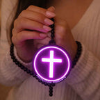 Hand holding a purple jesus protection pendant with a cross symbol